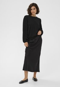 Sort striktrøje med ribbet ærmer, parret med en sort satin midi-nederdel og sorte flade sko med sløjfedetaljer. Generelt glat tekstur.