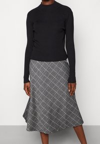 Černý žebrovaný pletený svetr s vysokým límcem v kombinaci se šedou kostkovanou rozšířenou sukní s bílými liniemi a hladkou texturou.