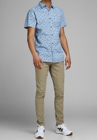 Short-sleeve blue shirt with a repeated small pattern, paired with beige pants and white sneakers with black accents.