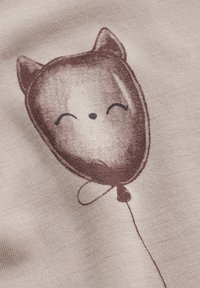Bomullstyg med en tecknad, brun ballong formad som ett katthuvud, med leende ögon och näsa, på en ljus beige bakgrund.