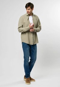 Camisa de manga larga beige claro con un diseño de botones, combinada con jeans de mezclilla azul y zapatillas de ante marrón. Look simple y casual.