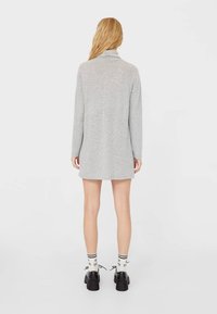 Graues, langärmliges Kleid mit Kragen aus weichem Stoff. Es hat eine lockere Passform und reicht bis zur Mitte des Oberschenkels, kombiniert mit schwarzen Plateau-Schuhen und gestreiften Socken.