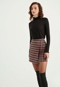 Schwarzes Rollkragenoberteil kombiniert mit einem rosa Hahnentrittmuster-Minirock. Der Rock hat einen asymmetrischen Saum und wird durch transparente schwarze Strumpfhosen und kniehohe Stiefel ergänzt.