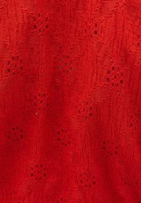 Tessuto rosso testurizzato con un motivo floreale caratterizzato da ritagli intricati e una superficie leggermente stropicciata, che crea profondità e interesse visivo.