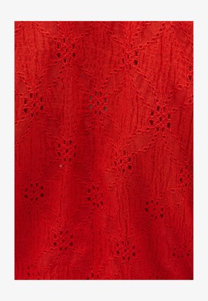 Tissu texturé rouge présentant un motif floral avec des découpes élaborées et une surface légèrement froissée, créant de la profondeur et un intérêt visuel.