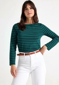 Langærmet top med grønne og marineblå striber og rund halsudskæring, kombineret med hvide bukser med høj talje og et brunt bælte. Blødt stof.