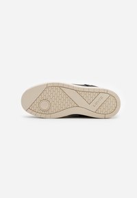 Semelle de sneaker noire présentant un design en caoutchouc texturé, semelle intermédiaire beige clair avec une marque en relief et un détail de logo circulaire.