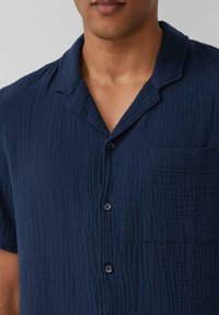 Marineblaues Kurzarmshirt aus strukturiertem Stoff mit einem kragenförmigen Ausschnitt, einer Brusttasche und einer durch Knöpfe verschließbaren Vorderseite.