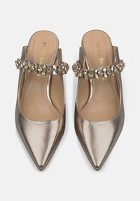 Mules metálicos dorados sin tacón con punta puntiaguda, que presentan una tira decorada con rhinestones claros. Textura de cuero suave y diseño minimalista.