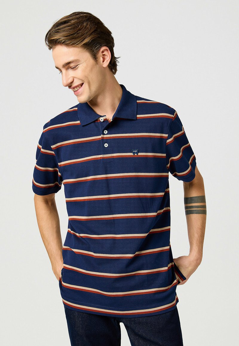 Mörkblå polo t-shirt med horisontella ränder i röd och beige. Har krage och tre knappar vid halsen, med en liten logotyp på bröstet.