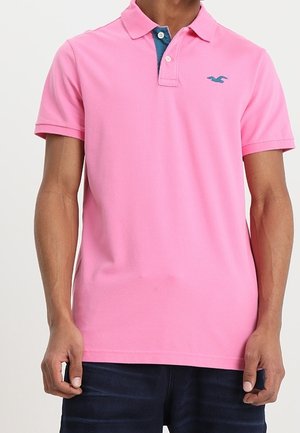Rosa Polo-Shirt aus Baumwolle, mit einer Zwei-Knopf-Leiste, kontrastierendem blauen Kragen und einem kleinen blauen Logo auf der Brust.