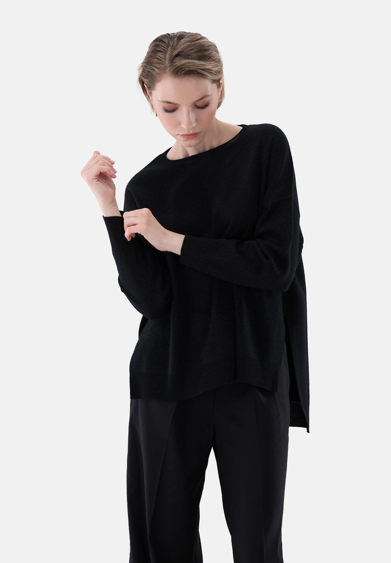 Schwarzer, übergroßer Strickpullover mit langen Ärmeln und rundem Ausschnitt, der eine weiche Textur und eine entspannte Passform aufweist, kombiniert mit schwarzen Hosen.