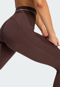 Brown high-waisted leggings with a smooth texture and seam detailing, featuring a narrow white accent band at the waist.