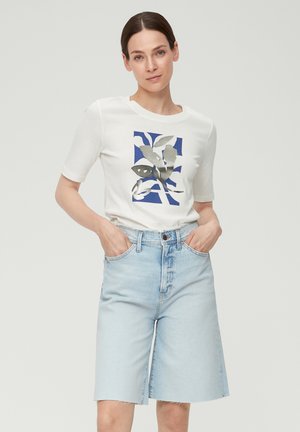 T-shirt blanc à manches courtes avec un motif de feuilles métalliques sur fond bleu, associé à un short en denim taille haute bleu clair avec des bords bruts.