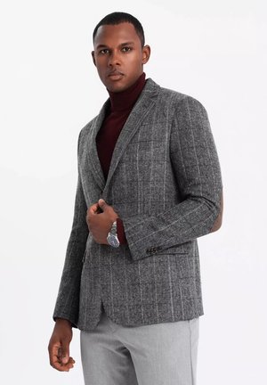 Gray herringbone blazer with a subtle check pattern, featuring notch lapels and a single button closure, worn over a burgundy turtleneck.