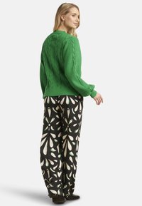 Green cable-knit sweater paired with black patterned wide-leg pants featuring white and green designs. Model stands in a neutral background.