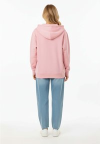 Felpa con cappuccio rosa dal fit rilassato, con maniche a costine e orlo, abbinata a pantaloni a gamba larga di un blu chiaro e sneakers bianche.