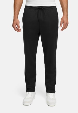 Schwarze Jogginghosen aus weichem Stoff, mit einem elastischen Bund und Kordelzug, geradem Schnitt und seitlichen Taschen. Getragen mit weißen Sneakers.