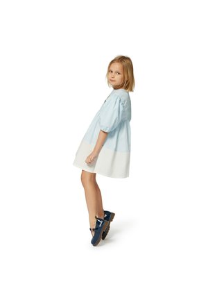 Robe bleu clair avec des manches bouffantes, un ourlet blanc et des détails brodés ; portée avec des chaussures bleu marine à semelle marron.