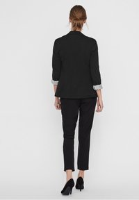 Czarna elegancka marynarka z podwiniętymi jasnoszarymi mankietami, w połączeniu z czarnymi spodniami slim fit i czarnymi szpilkami. Prosty i czysty design.