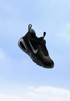 Une chaussure de sport Nike noire avec un Swoosh gris flotte sur fond de ciel bleu parsemé de nuages.