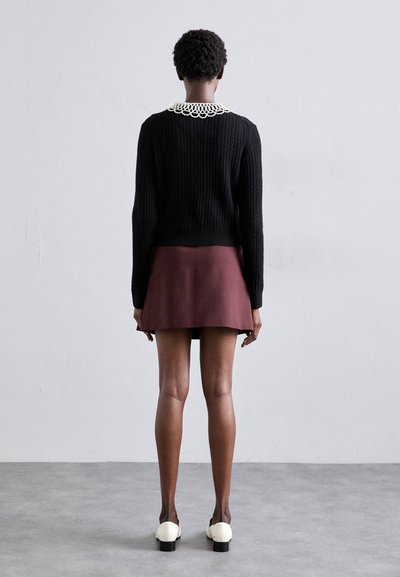Pull en maille noire avec un col blanc à volants, associé à une mini-jupe bordeaux et des chaussures à talons bicolores.