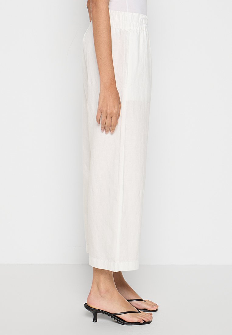 Weiße Leinen-Cropped-Hosen mit elastischem Bund, im lockeren Schnitt und mit geradem Bein. Kombiniert mit schwarzen Riemchensandalen.