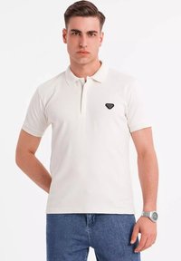 Hvid polo t-shirt med et enkelt design, korte ærmer, krave og sort logo-emblemer på venstre bryst. Kombineret med lyseblå denim jeans.