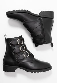 Svarta ankelskor i slät läder, med tre silverfärgade spännen, nitar, en sidodragkedja och en kraftig gummisula.