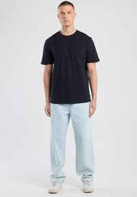 Camiseta de cuello redondo negra de manga corta, combinada con jeans de pierna ancha de color azul claro y zapatillas blancas. Diseño sencillo y casual.