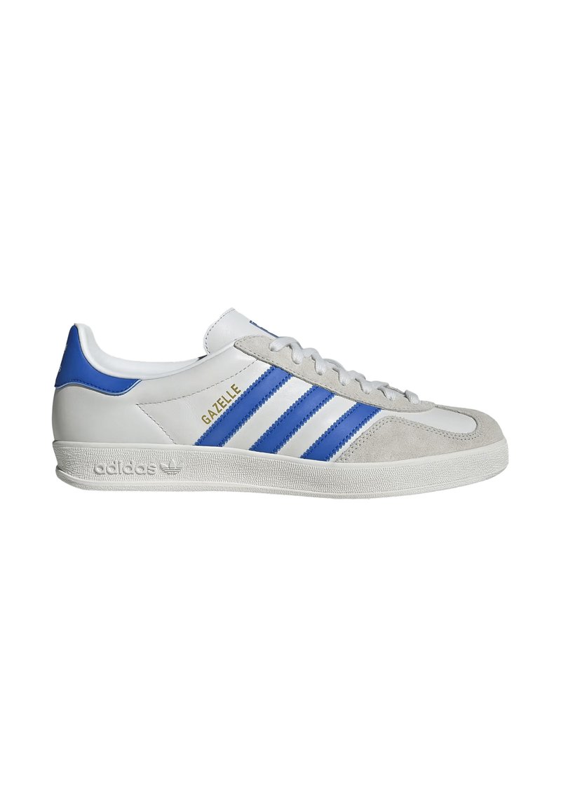 Baskets Adidas Gazelle blanches avec des rayures bleues et un embout en suède gris, dotées d'une semelle blanche texturée et d'un logo doré sur le côté.