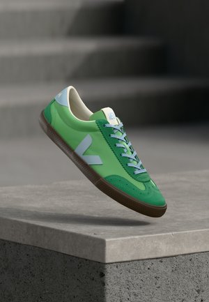 Zielone skórzane sneakersy o gładkiej fakturze, z jasnoniebieskimi akcentami, brązową gumową podeszwą i kontrastującymi sznurowadłami.