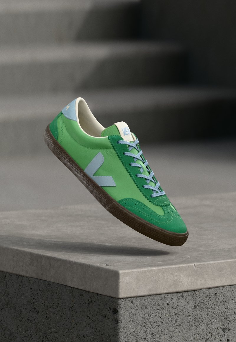 Baskets en cuir vert à texture lisse, avec des accents bleu clair, une semelle en caoutchouc marron et des lacets contrastants.