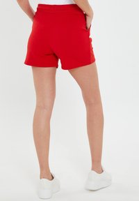 Pantaloni corti rossi in cotone con vita elastica, tasche laterali e una vestibilità comoda. Tekstura liscia con orlo pulito alle aperture delle gambe.
