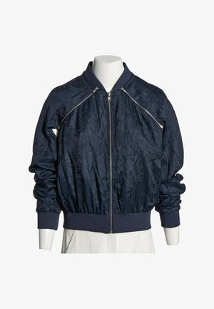 Blouson bomber bleu marine foncé avec fermeture éclair frontale, poignets et ceinture côtelés, et fermetures éclair diagonales décoratives près des épaules.
