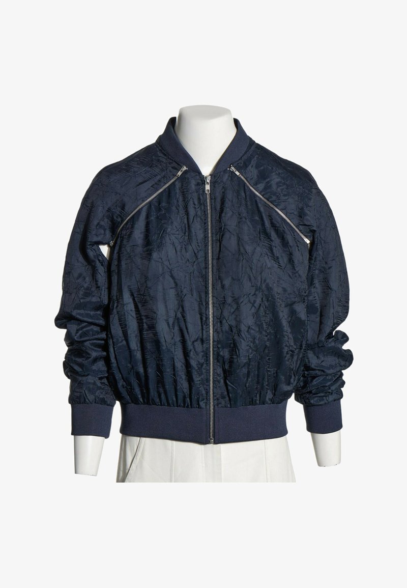 Blouson bomber bleu marine foncé avec fermeture éclair frontale, poignets et ceinture côtelés, et fermetures éclair diagonales décoratives près des épaules.