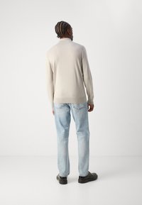 Suéter de punto beige claro con dobladillo acanalado, combinado con jeans rectos de color azul claro y zapatos negros, visto desde la parte posterior.