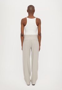 Lichtgrijze wijde broek met een gladde textuur, voorzien van een rechte tailleband en twee achterzakken. Gecombineerd met een aansluitend wit tanktop.