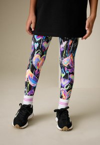 Farebné legíny srdiečkovým vzorom v ružovej, modrej a zelenej na čiernom pozadí; elastická tkanina; v kombinácii s čiernymi teniskami.