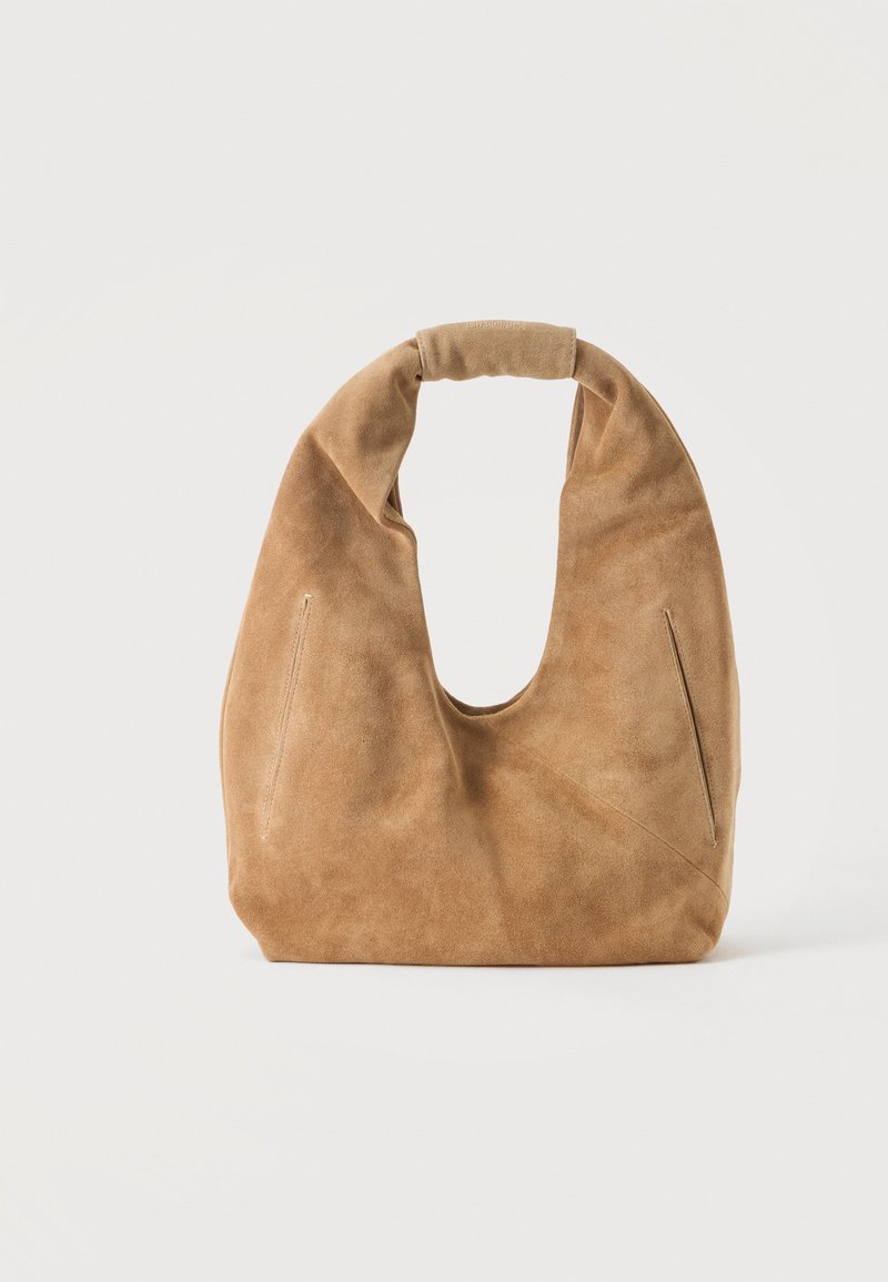 Sac hobo en daim marron clair doux avec poignée arrondie et poches latérales discrètes sur fond uni clair.