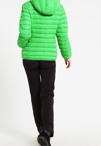 Zielona puchowa kurtka z poziomym przeszyciem i kapturem, w połączeniu z czarnymi spodniami. Kurtka ma błyszczące wykończenie i elastyczne mankiety.