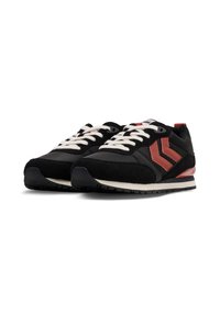 Czarne i czerwone buty sportowe z zamszową i tekstylną cholewką, gumową podeszwą, białymi sznurówkami i czerwonymi akcentami w kształcie chevronu po bokach.