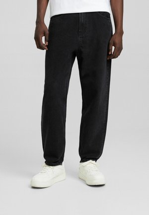 Jeans de mezclilla negra con corte recto, diseño de cinco bolsillos y detalles de costura sutiles. Combinados con zapatillas blancas.