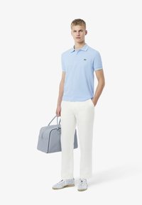 Ljusblå polo med kontrasterande krage, vita byxor, grå väska och ljusa sneakers. Har en grön logotyp på skjortan.