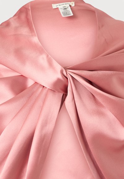 Tissu en satin rose torsadé en nœud au centre avec une étiquette de vêtement visible à l'encolure à l'intérieur d'un vêtement.