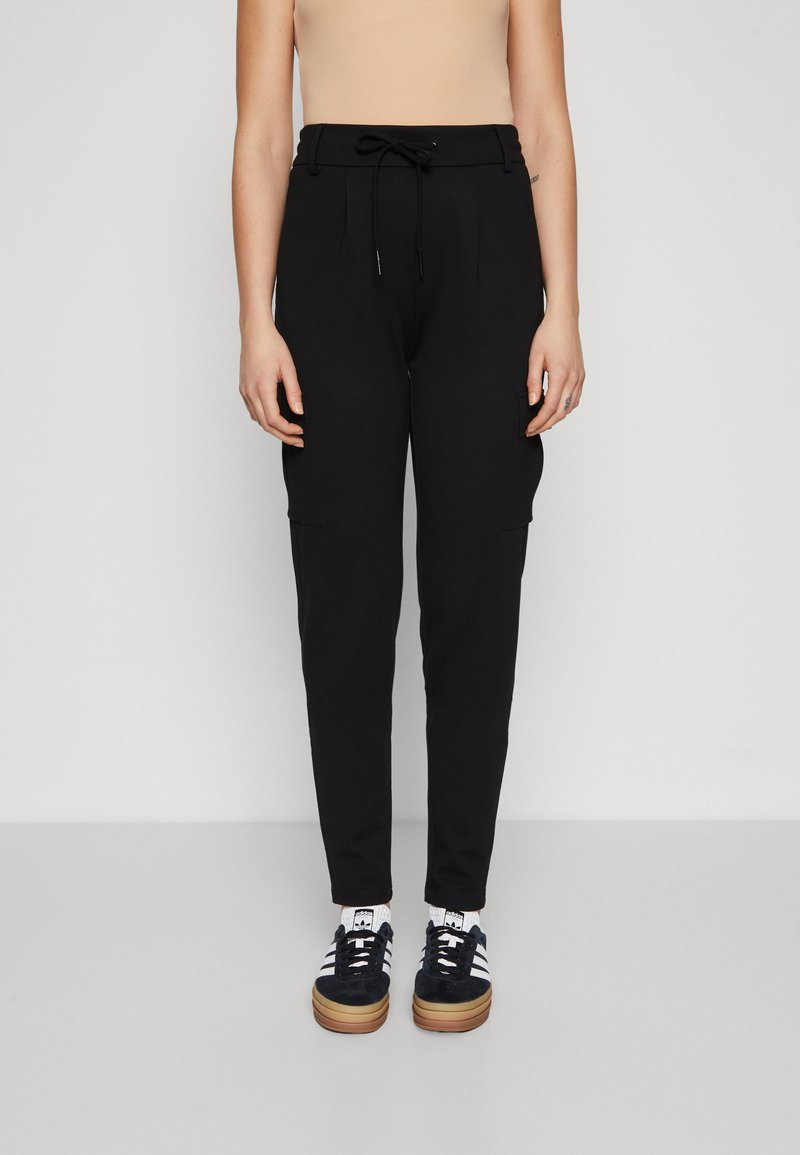 Schwarze Cargo-Hosen mit einem Kordelzugbund, Seitentaschen und einer schmalen Passform, kombiniert mit dunklen Sneakers und weißen Socken.