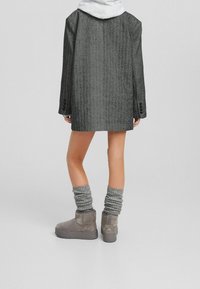 Blazer oversize grigio con texture e maniche lunghe, abbinato a calze lunghe grigie a coste e stivaletti color talpa.