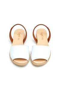 Sandalias deslizantes de cuero blanco con una tira ancha y una correa marrón en el tobillo. Textura natural en la suela, con una ligera plataforma.