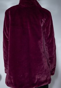 Abrigo de forro polar burdeos con una textura suave y aterciopelada. Presenta un cuello y un ajuste relajado, cubriendo las caderas con detalles mínimos.