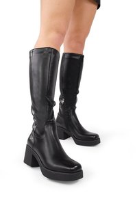 Botas de cuero negras hasta la rodilla con un tacón cuadrado, que cuentan con una textura suave, cremallera lateral y puntera redondeada.